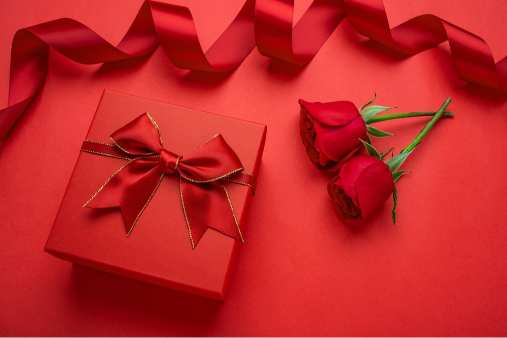 Red gift-wrapped present and roses A Valentine's Day present wrapped in red wrapping paper with a red bow, next to red roses on a red background.