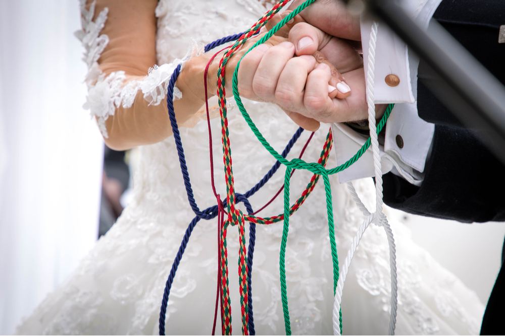 A couple during their wedding with ropes tied around their hands in a tradition called handfasting.