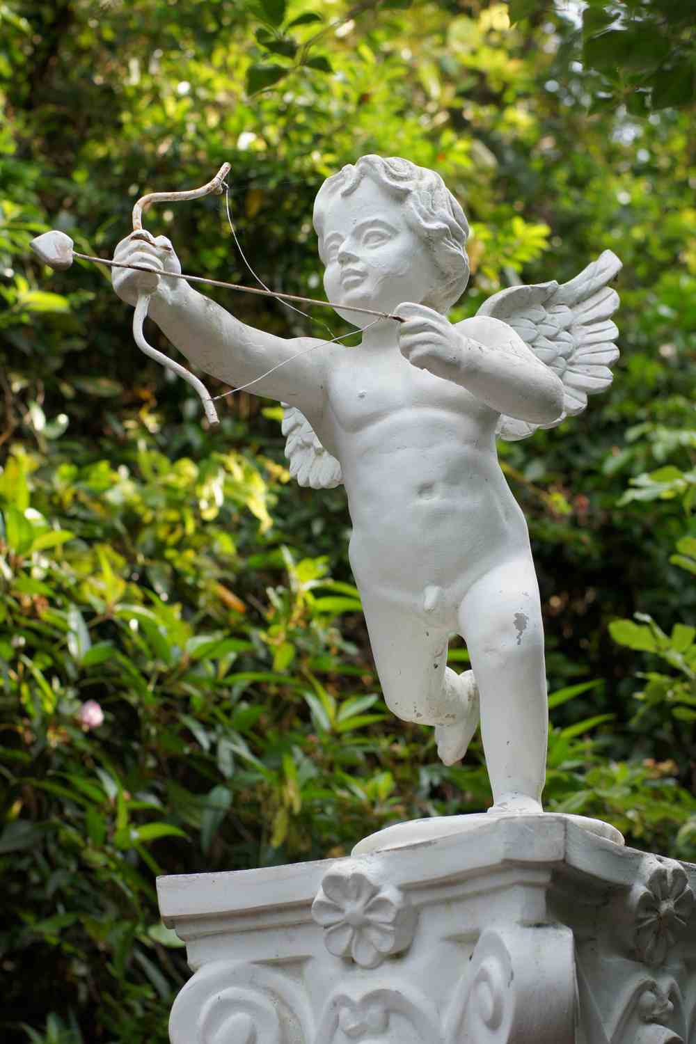 A stone statue of Cupid depicted as a winged baby holding a bow and arrow.