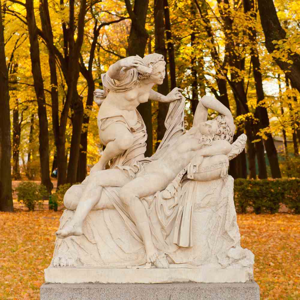 Statue of the story of Cupid and Psyche surrounded by trees A statue of the Cupid and Psyche story during the fall, with trees dropping yellow leaves around it.
