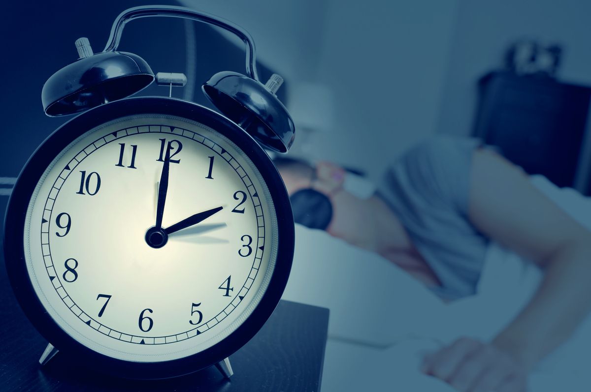 Person sleeping and alarm clock A person sleeping in a bed with a blindfold, with an alarm clock at 2am for daylight saving time in the foreground of the photo.