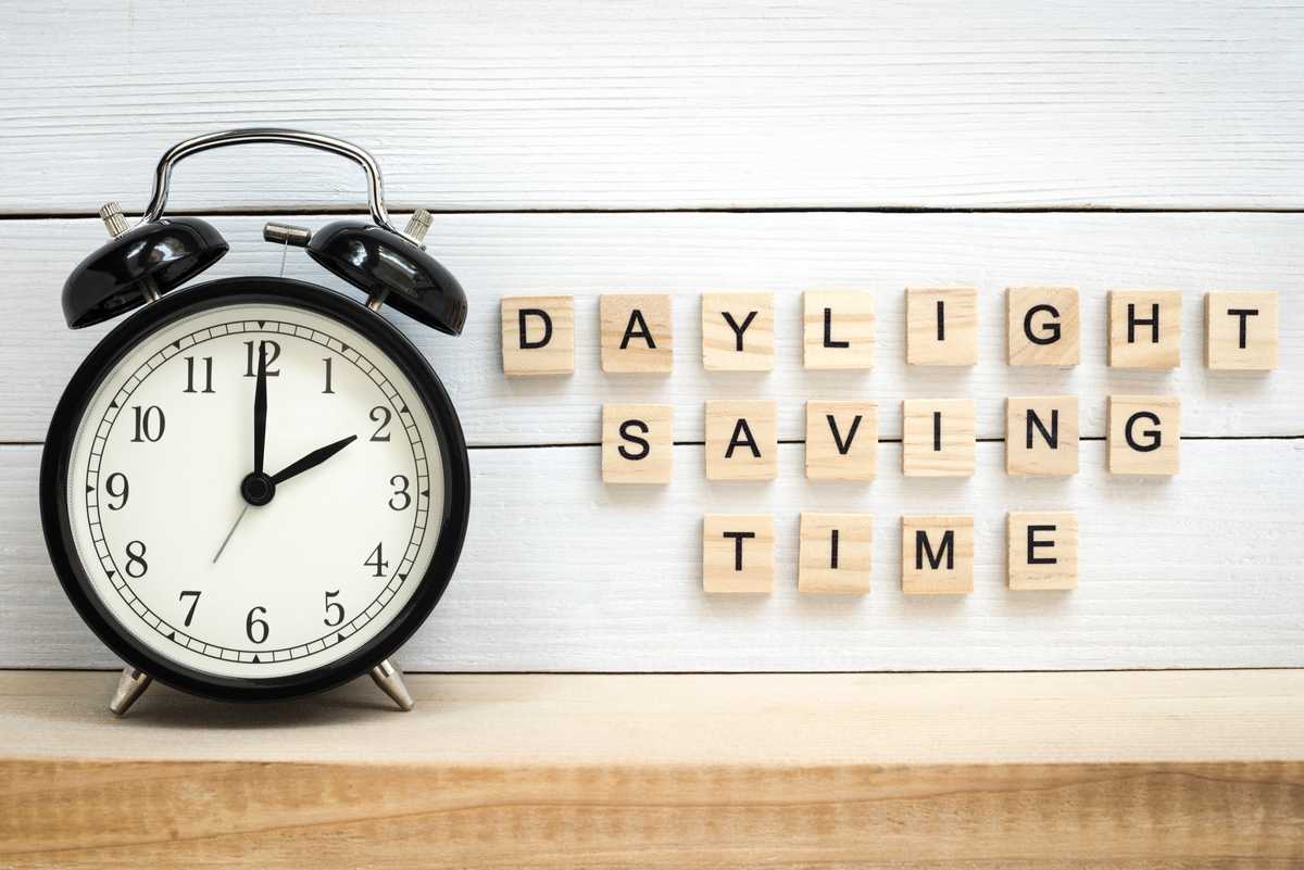 Alarm clock and scrabble tiles An alarm clock on a wooden table with scrabble tiles reading "daylight saving time" next to it.