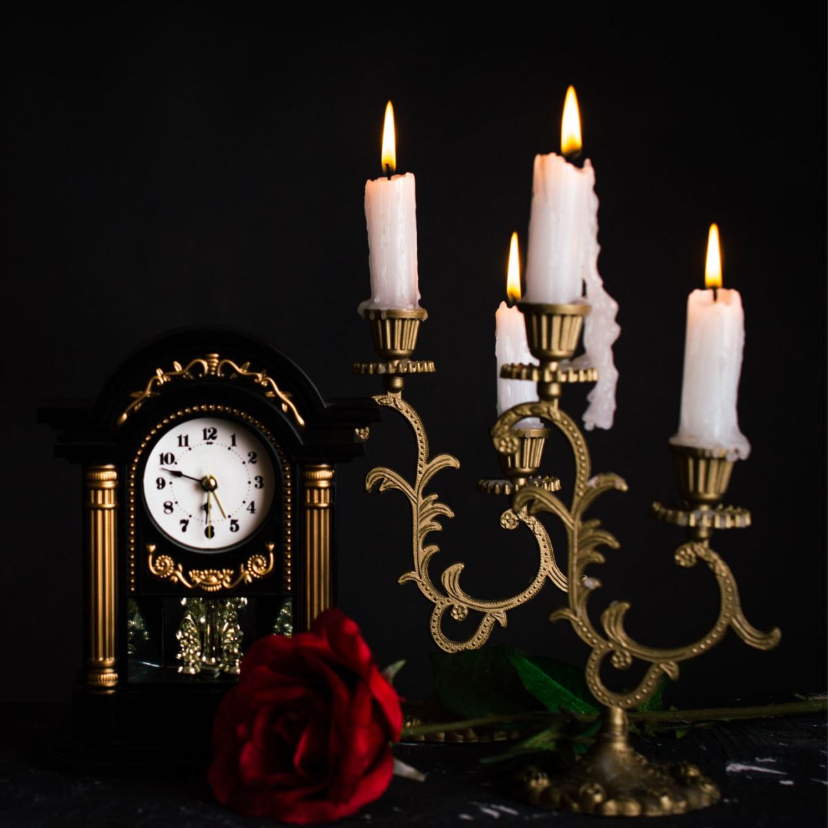 Clock, candles and rose An old fashioned clock, candelabra with lit candles and a red rose arranged together against a black background.