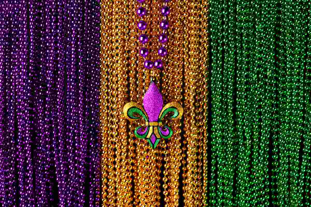 Beads in the colors of Mardi Gras, purple, gold and green, with a fleur de lis necklace on top of them.