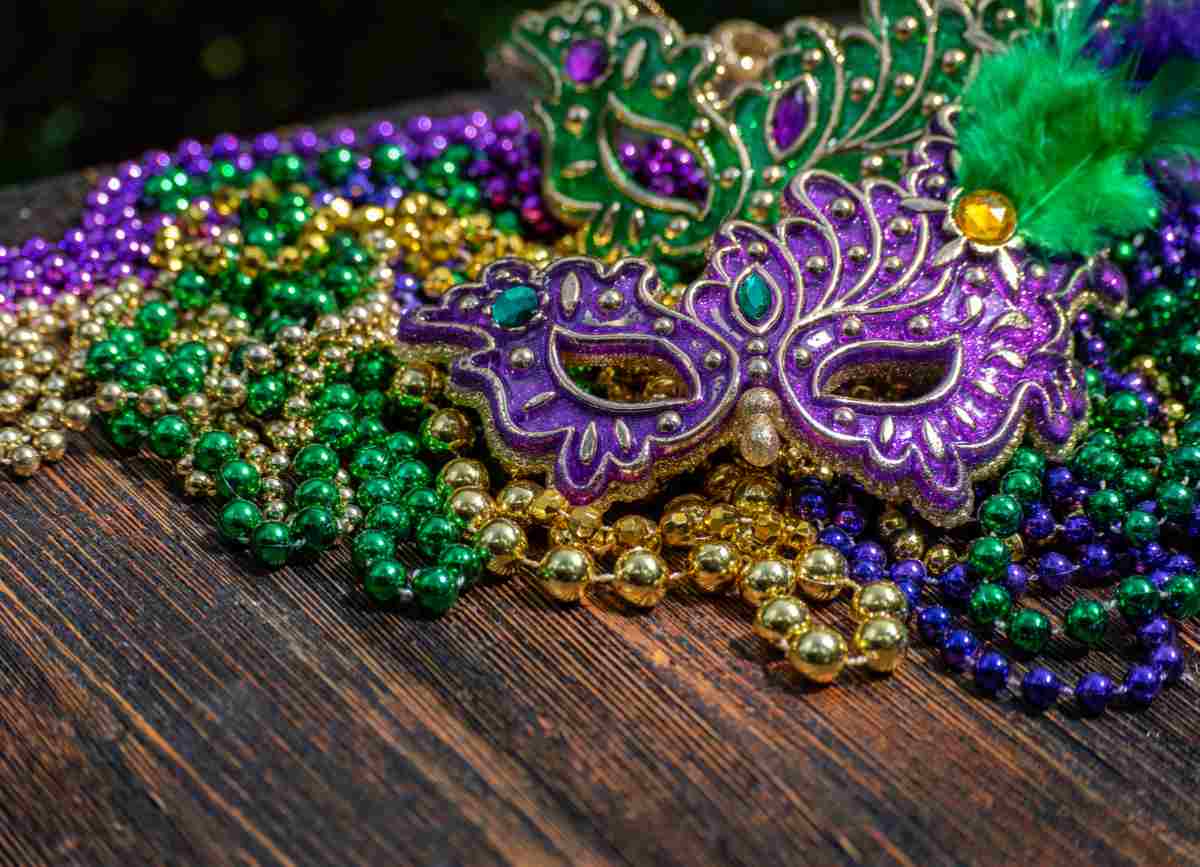 Mardi Gras beads and mask Mardi Gras beads and a Mardi Gras mask on a wooden table to honor the classic Mardi Gras traditions.