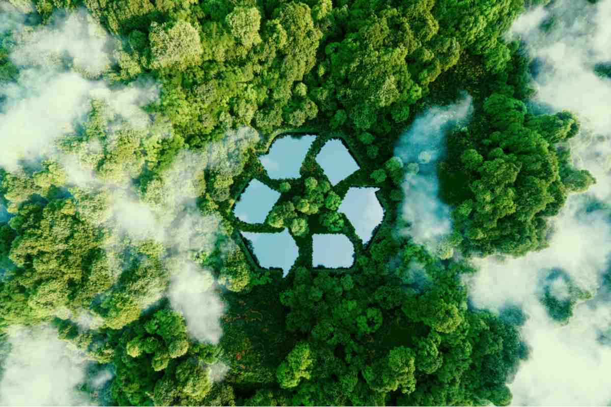 An overhead shot of a forest with patches of fog, and a recycle symbol in the center made of lakes.