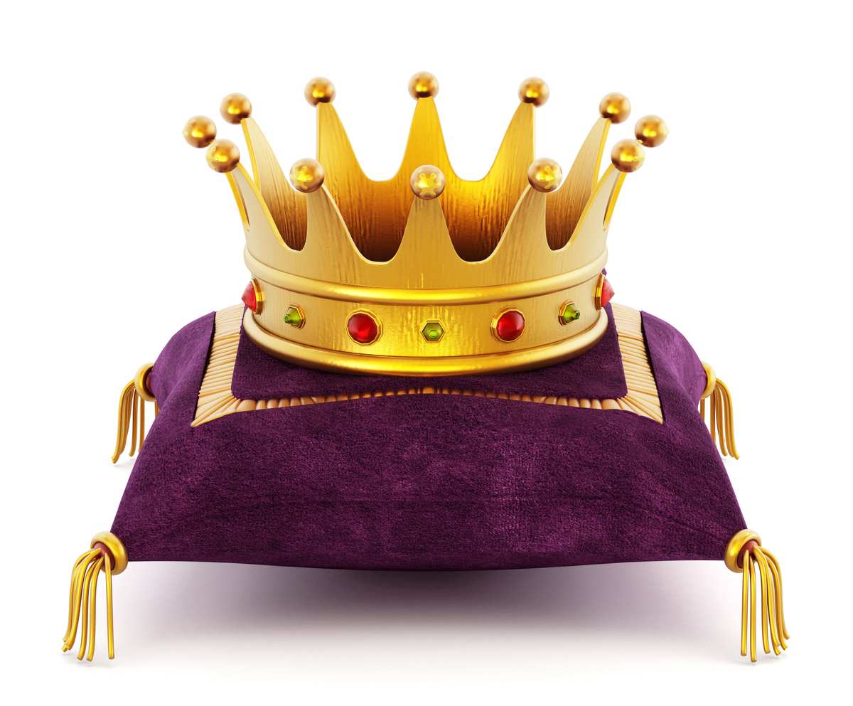 A gold crown with red and white jewels on it, sitting on a purple pillow with four gold tassels on each corner.