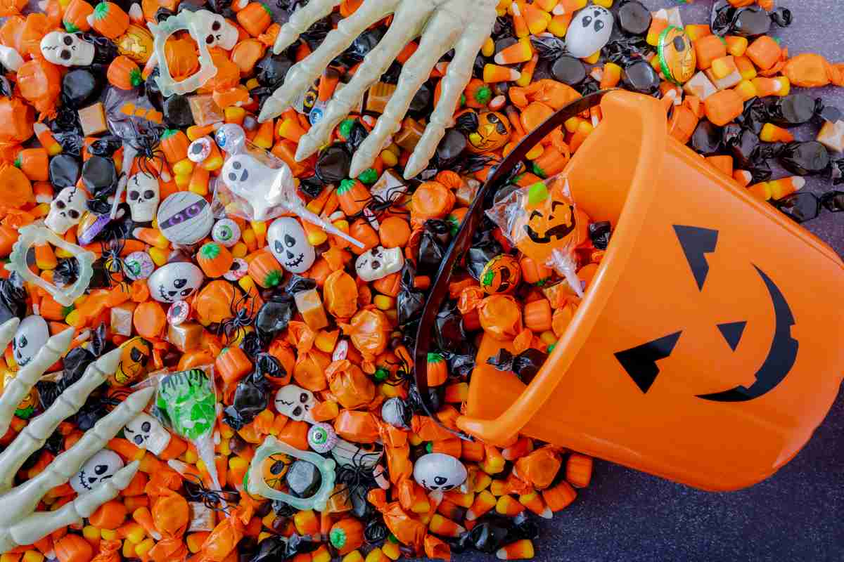 Bucket of Halloween candy A plastic jack-o-lantern bucket with candy spilling out of it, and two plastic skeleton hands on it.