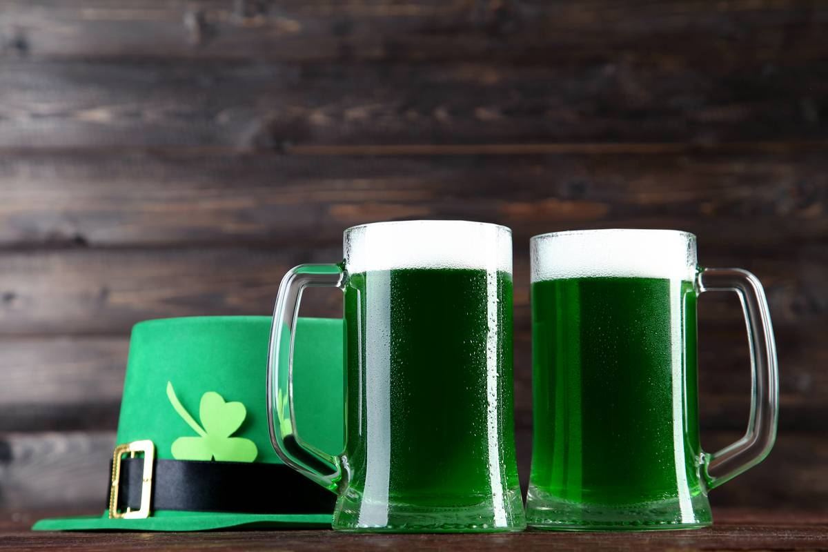 Green beer Two pints of green beer next to a green hat with black and gold buckle, and a shamrock tucked in to it against a wooden background to celebrate the symbols of St. Patrick's Day.