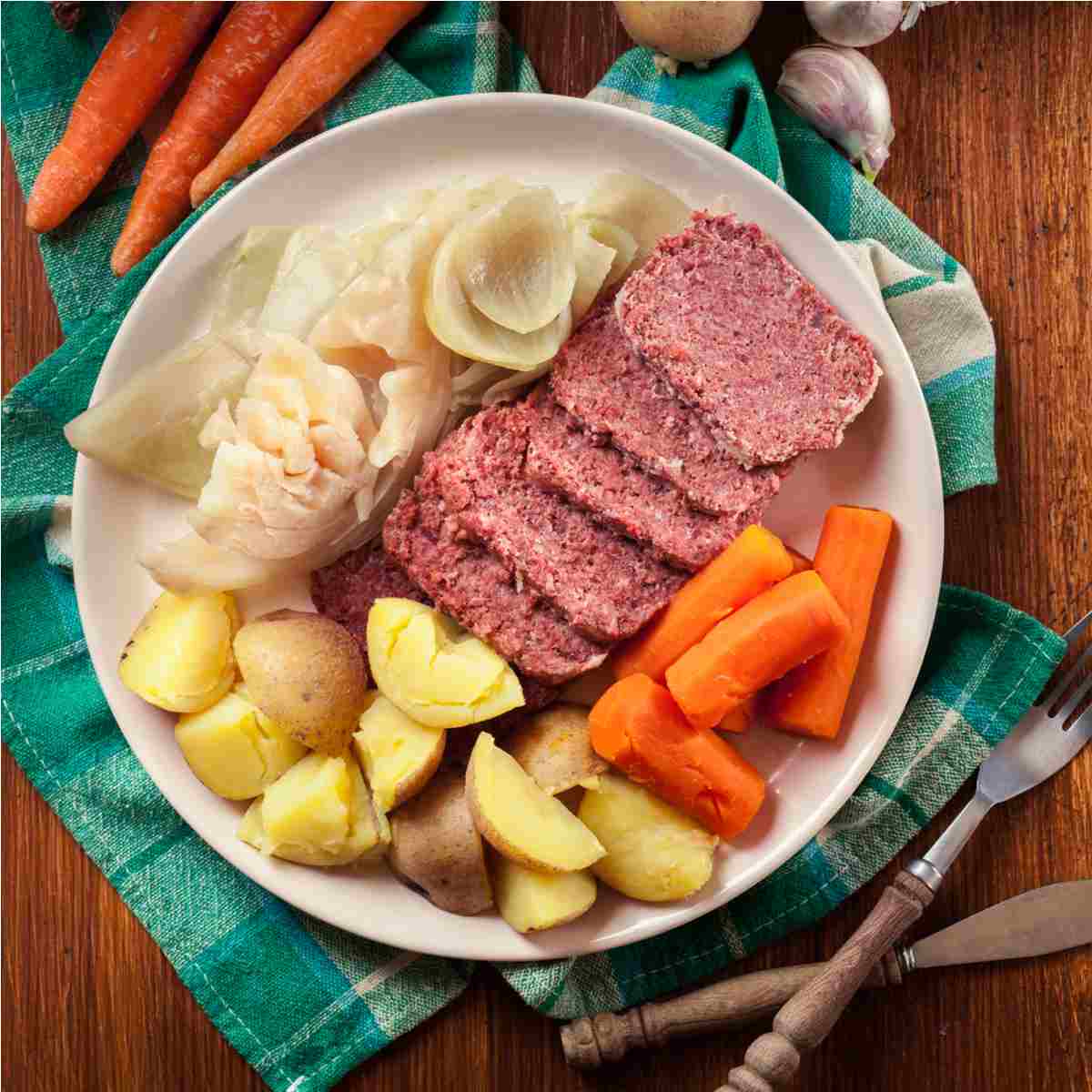 Corned beef and cabbage A plate of Irish corned beef and cabbage with potatoes and carrots on top of a green napkin next to a fork and knife.