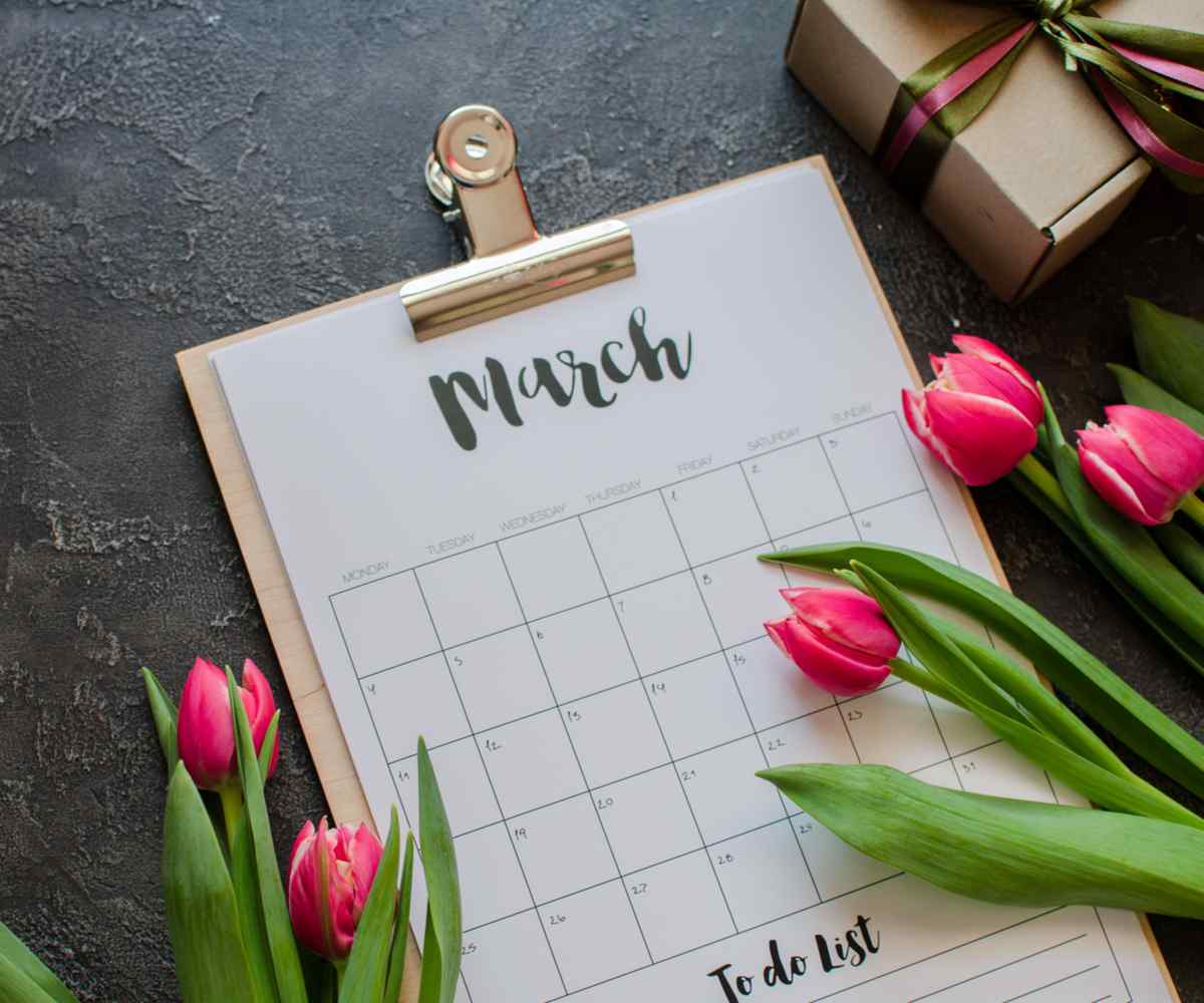 March calendar A calendar of March on a wooden clipboard surrounded by pink tulips and a wrapped box.