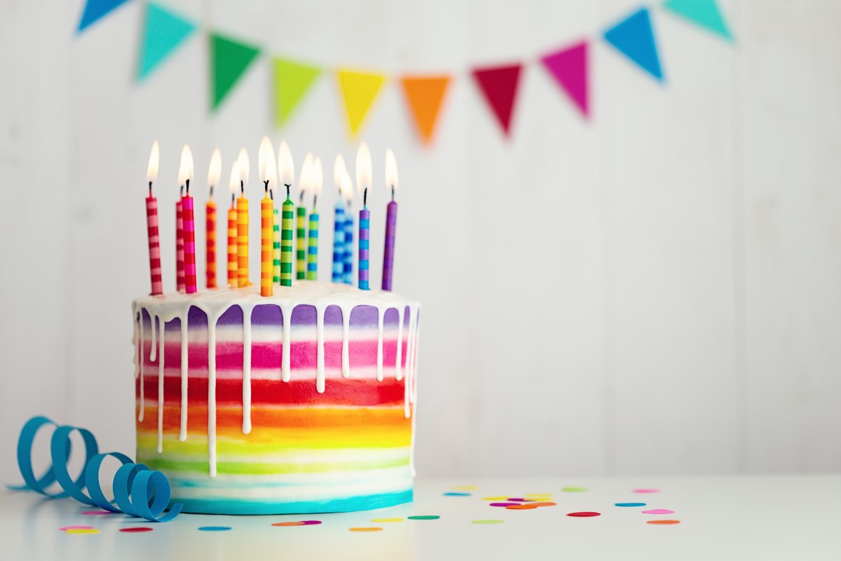 Rainbow cake with candles A rainbow cake with rainbow candles and a rainbow banner against a white background to celebrate National Find a Rainbow Day.