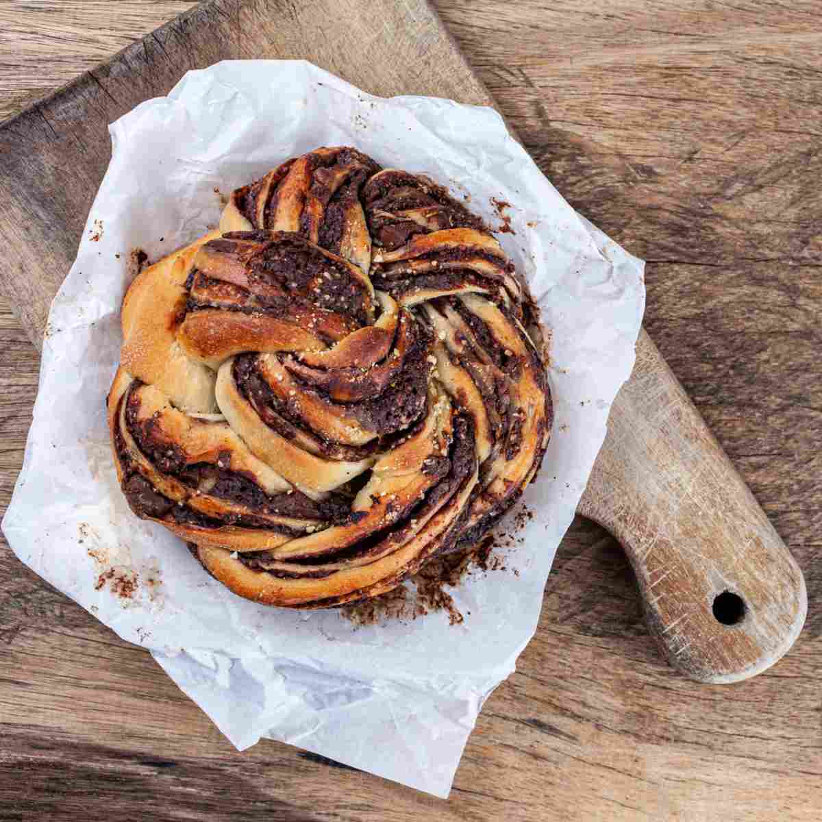 Polish Easter bread called babka A handmade chocolate babka (Polish Easter bread) on parchment paper on top of a wooden cutting board.