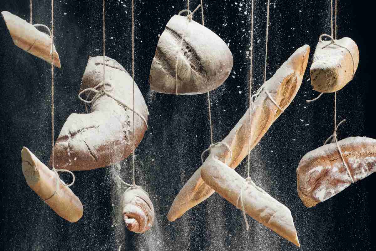 Hanging breads Different types of bread hanging from twine with flower falling off of them, the bread types include French baguettes and sourdough bread.