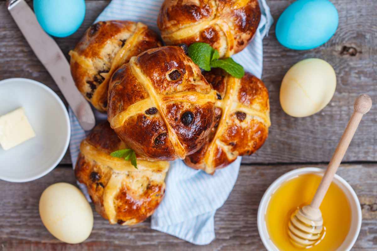 Easter eggs and hot cross buns Golden brown hot cross buns on a plate next to honey and Easter eggs to represent the meaning of hot cross buns for Easter.