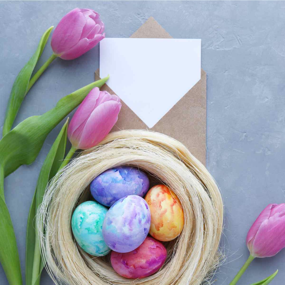 Dyed Easter eggs and note A small wicker basket of dyed Easter eggs next to tulips and a blank note in an envelope.