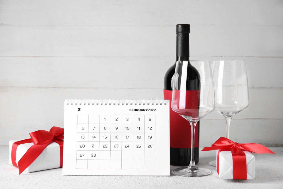 February calendar and wine A red wine bottle, two wine glasses, and a white box with a red bow on it next to a February calendar of national wine days.
