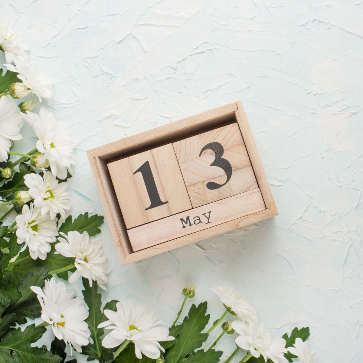 May 13 blocks Wooden blocks that read "May 13" next to white flowers to bring attention to May 13 national days.