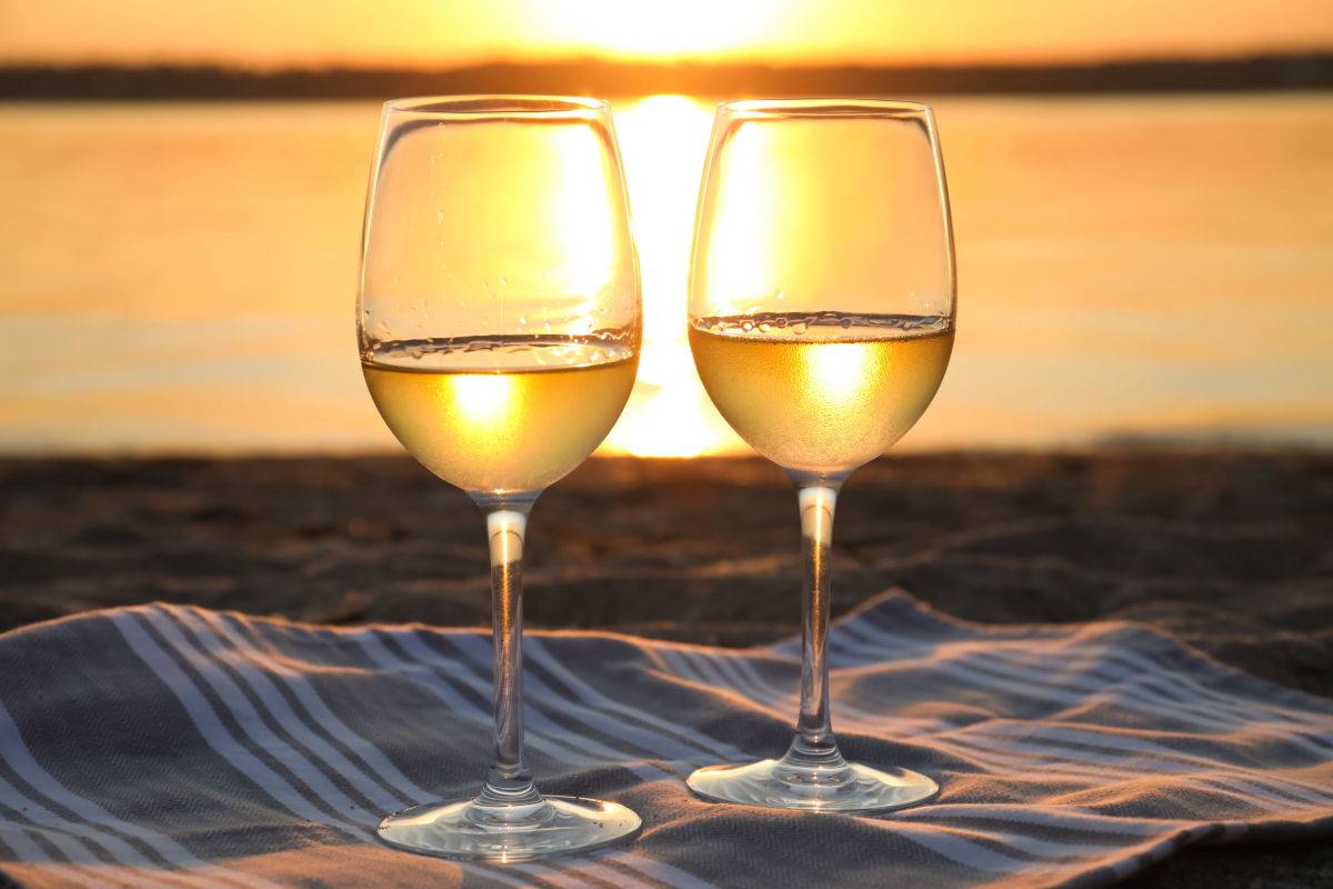 White wine at the beach Two white wine glasses on a blanket at a beach during sunset on National White Wine Day.