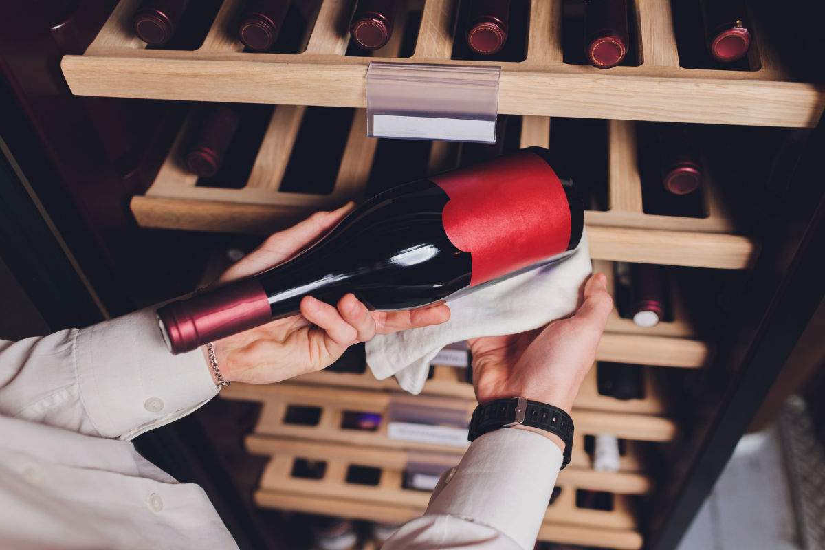 Red wine from storage A bottle of red wine at the ideal temperature for storing red wine being pulled out of a wooden wine storage rack by someone wearing a white long sleeved button down shirt.