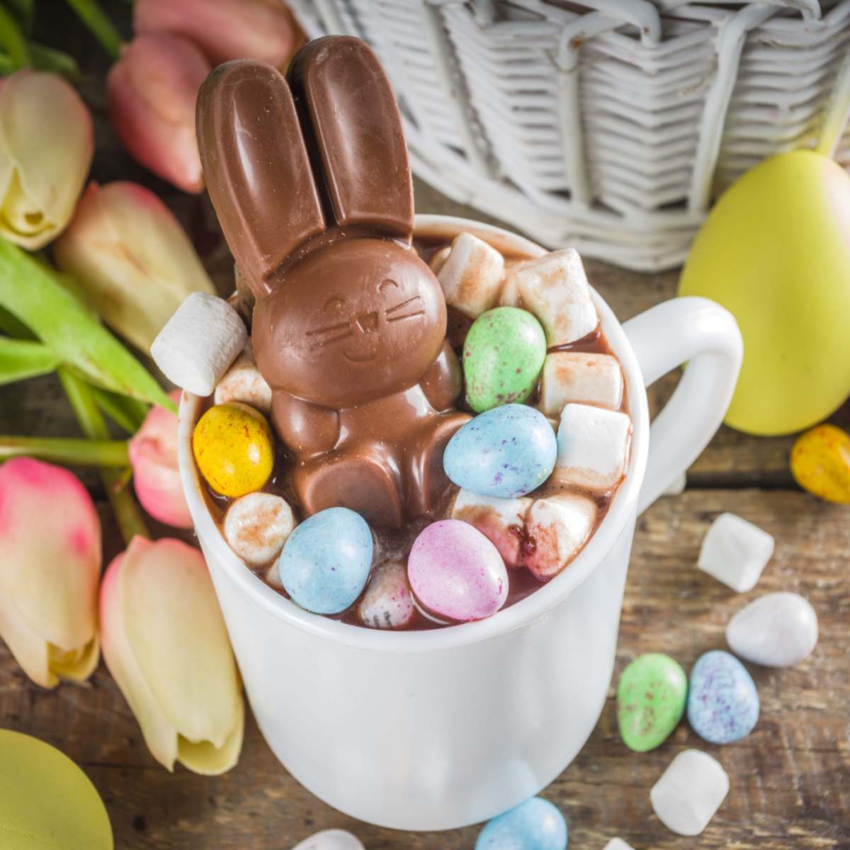 Chocolate bunny in mug of hot chocolate A chocolate bunny in a cup of hot chocolate during Easter, on a table surrounded by candies and tulips.