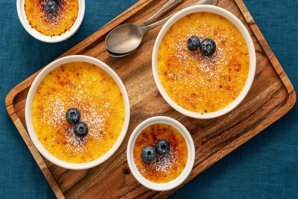 Creme brulee on cutting board Two large creme brulee and one small one on a cutting board with two spoons, each is topped with blueberries.