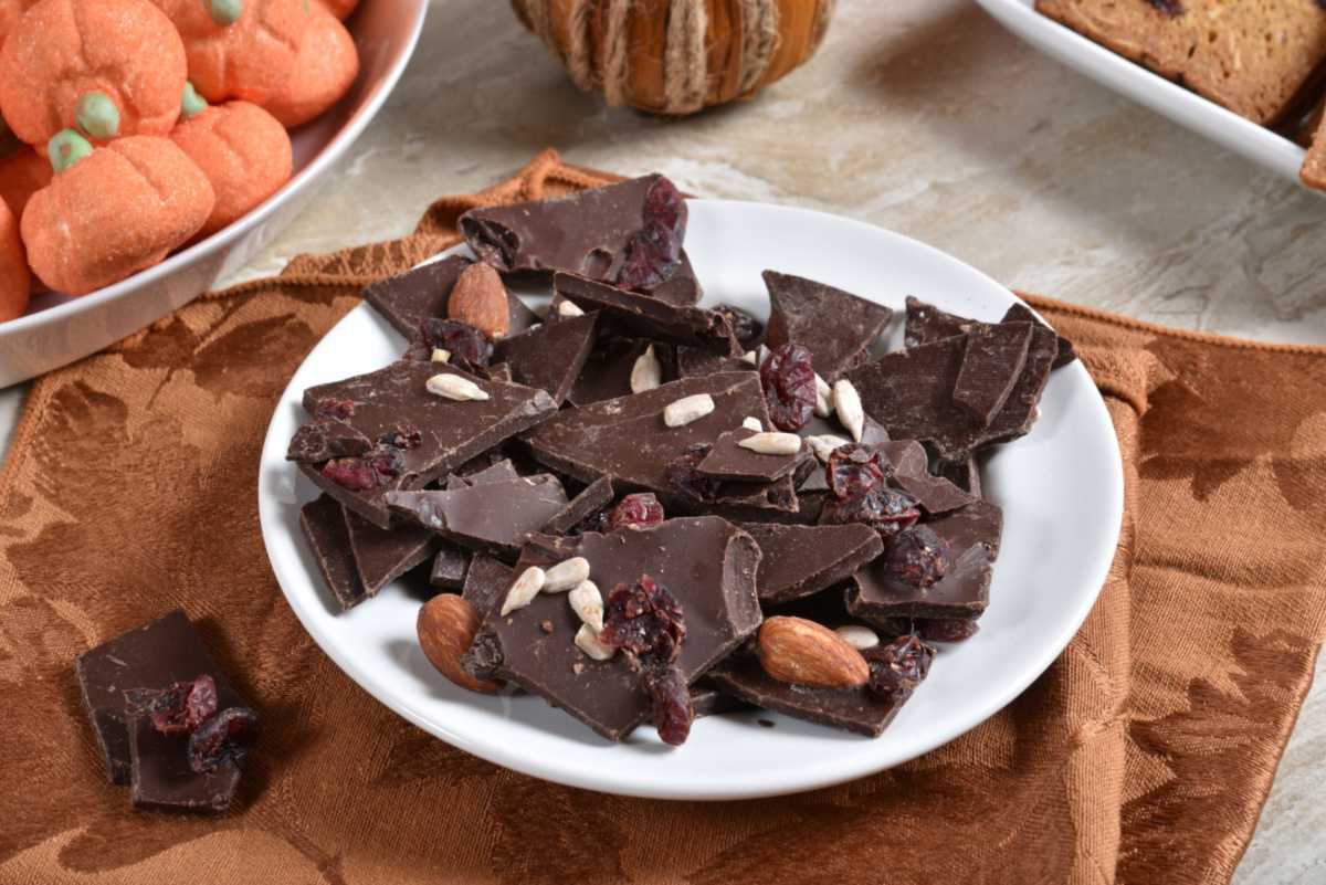 Chocolate almond bark Dark chocolate bark with almonds and dried fruit on a table with fall placemats underneath it.