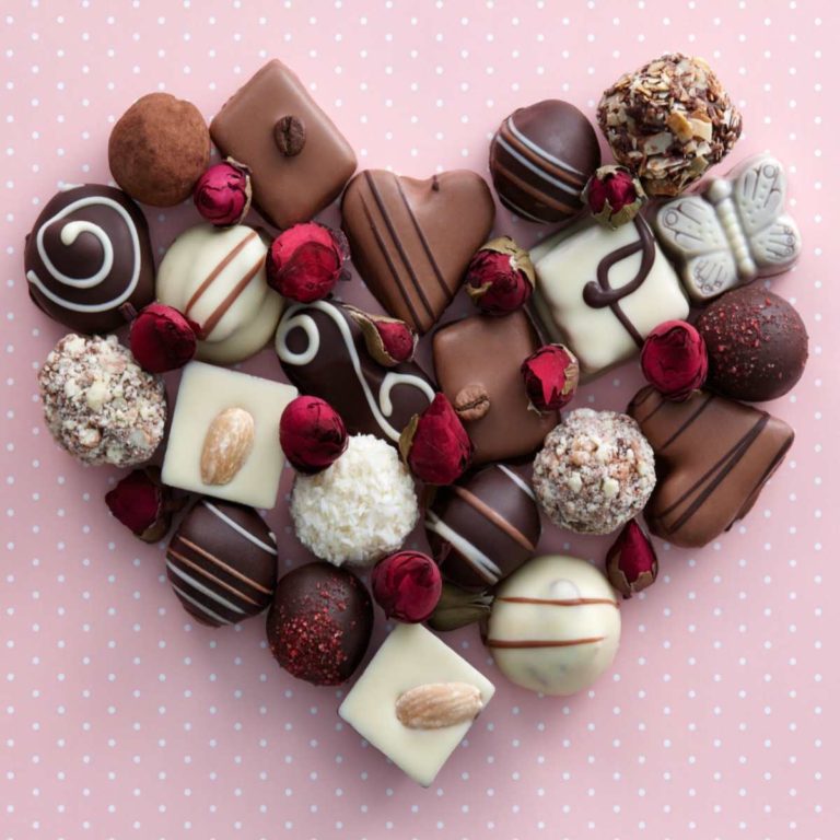 Dark chocolates, white chocolates, and milk chocolates in the shape of a heart against a pink background to represent the national chocolate days during the year.