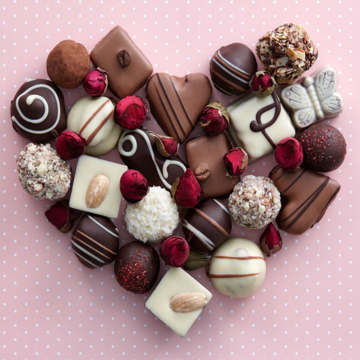 Chocolates in a heart shape Dark chocolates, white chocolates, and milk chocolates in the shape of a heart against a pink background to represent the national chocolate days during the year.