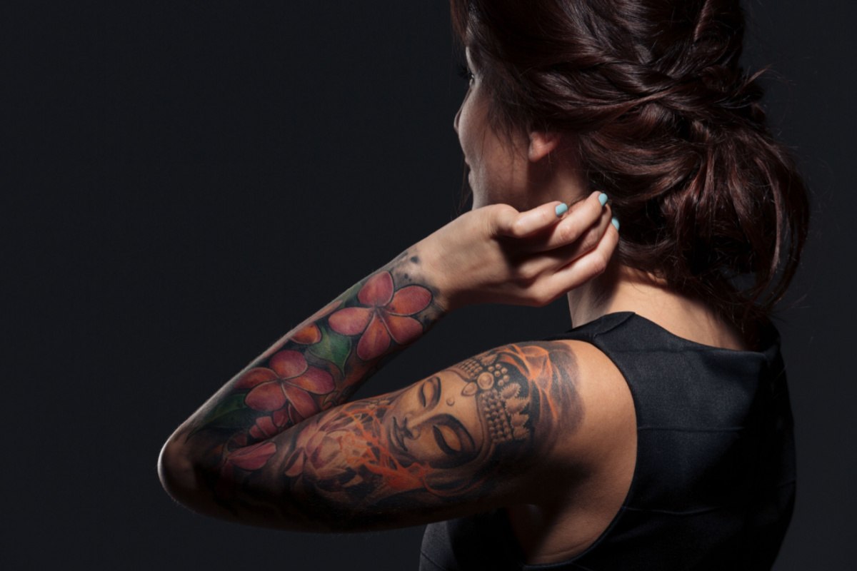 Woman with tattoo sleeve A brunette woman touching her hair with her left hand, showing off a full sleeve of tattoos on her left arm consisting of roses and a Buddha design.