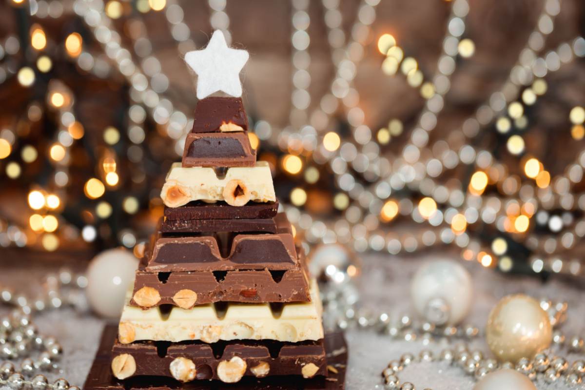 Chocolate bar tree shape Various chocolate bars stacked in the shape of a Christmas tree with twinkle lights in the background.