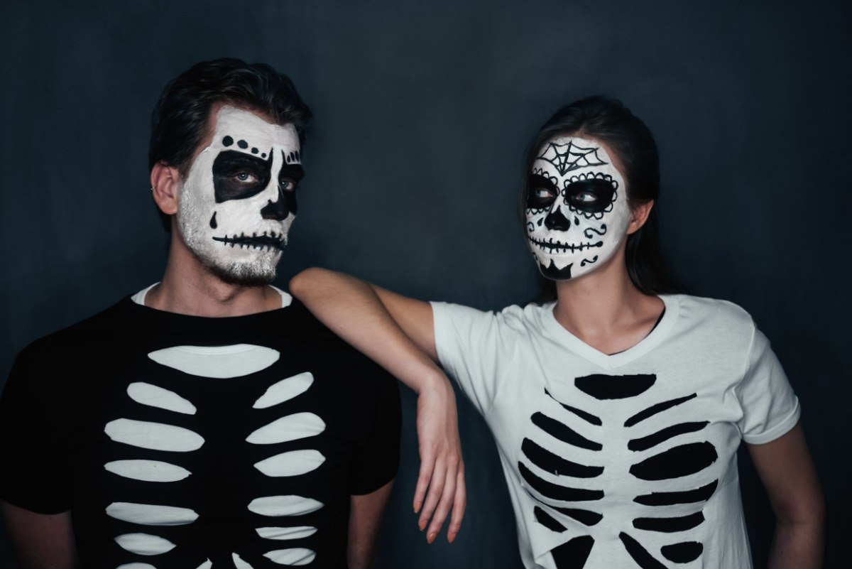 DIY skeleton costumes for couples A couple wearing DIY skeleton costumes with their faces painted too, the man on the left has a black shirt white a white skeleton outline cut out of it, and the woman on the right has a white shirt with a black skeleton outline cut out of it.