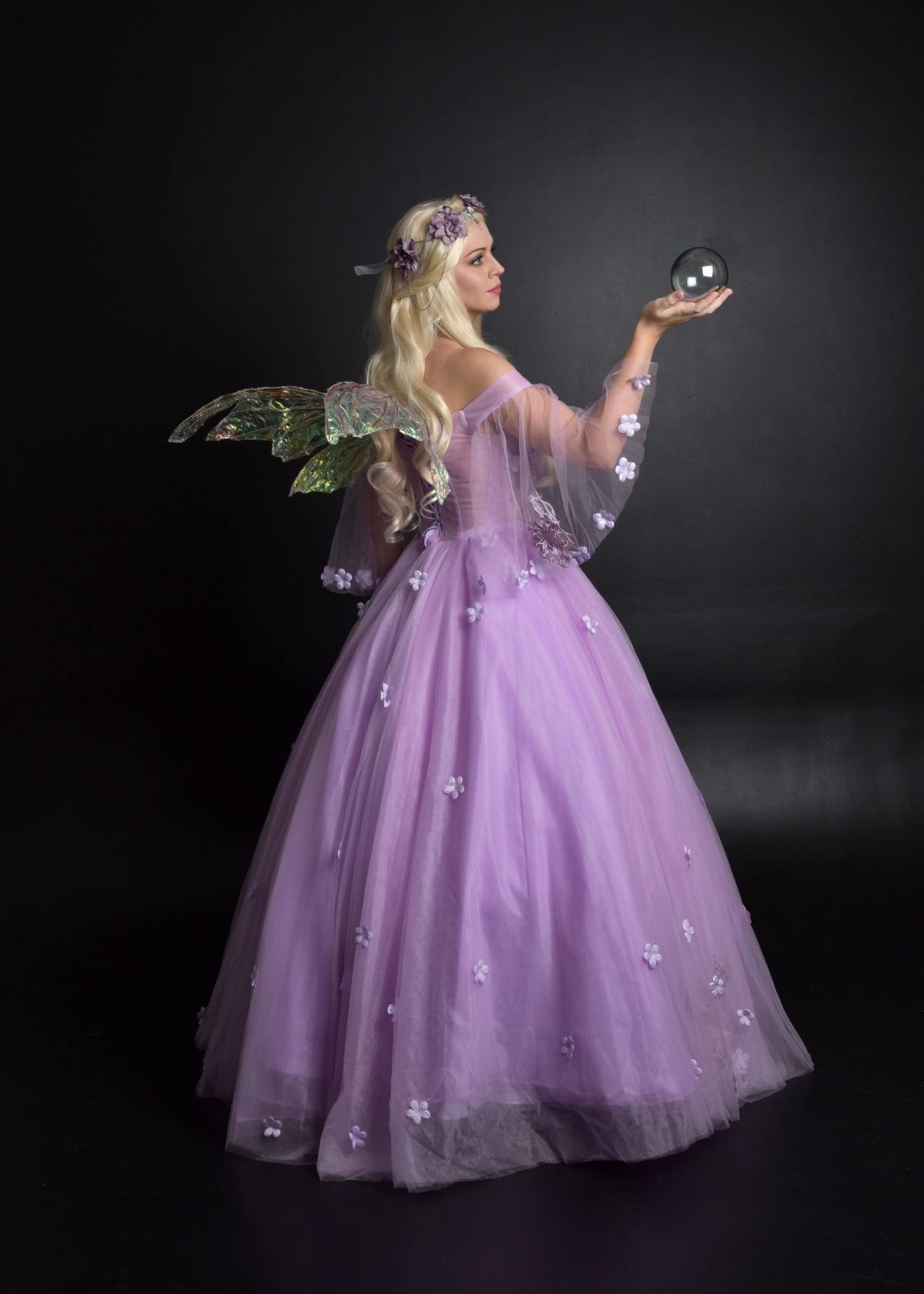 Homemade fairy costume A blonde woman wearing a diy fairy costume that's a purple dress, with faerie wings, and a flower crown holding a crystal ball.