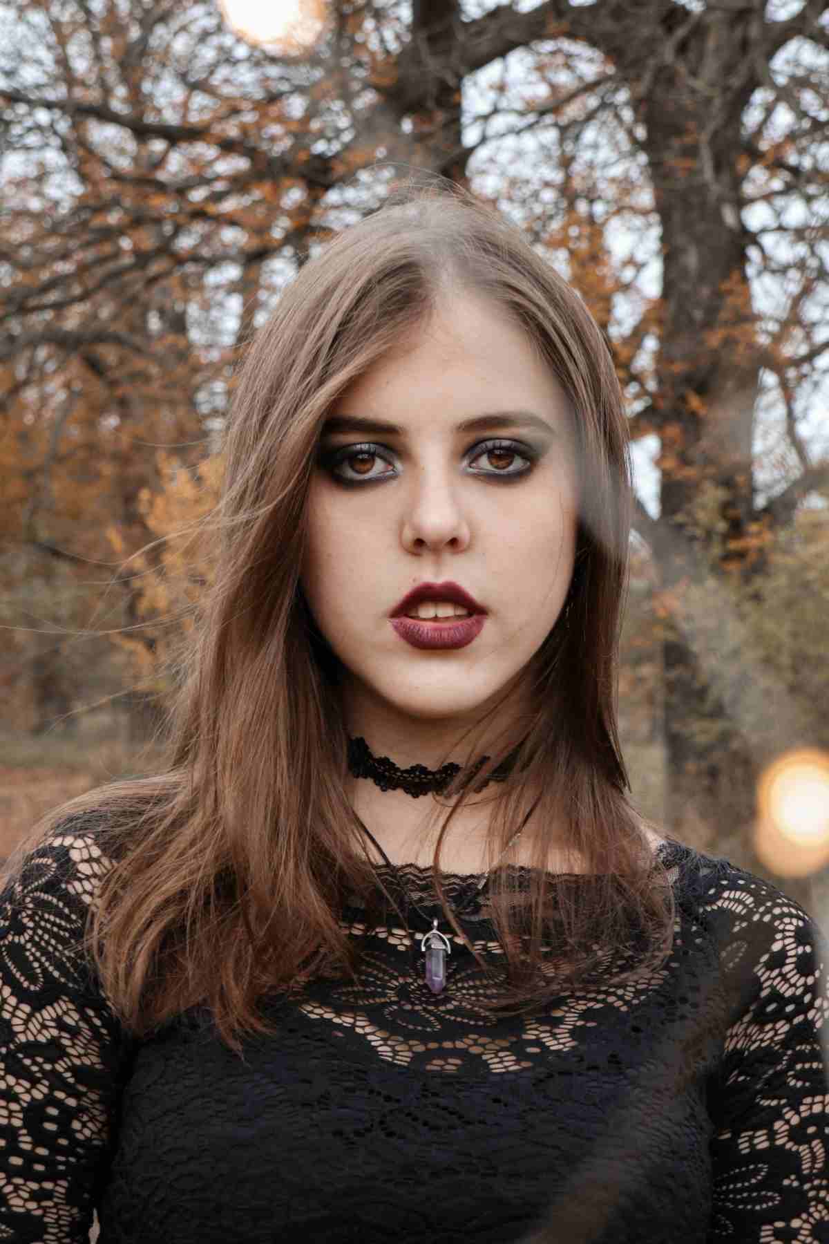 Gothic Halloween costume A girl dressed in a gothic Halloween costumes for adults, consisting of a lace top, dark eye makeup, and black jewelry in the woods.