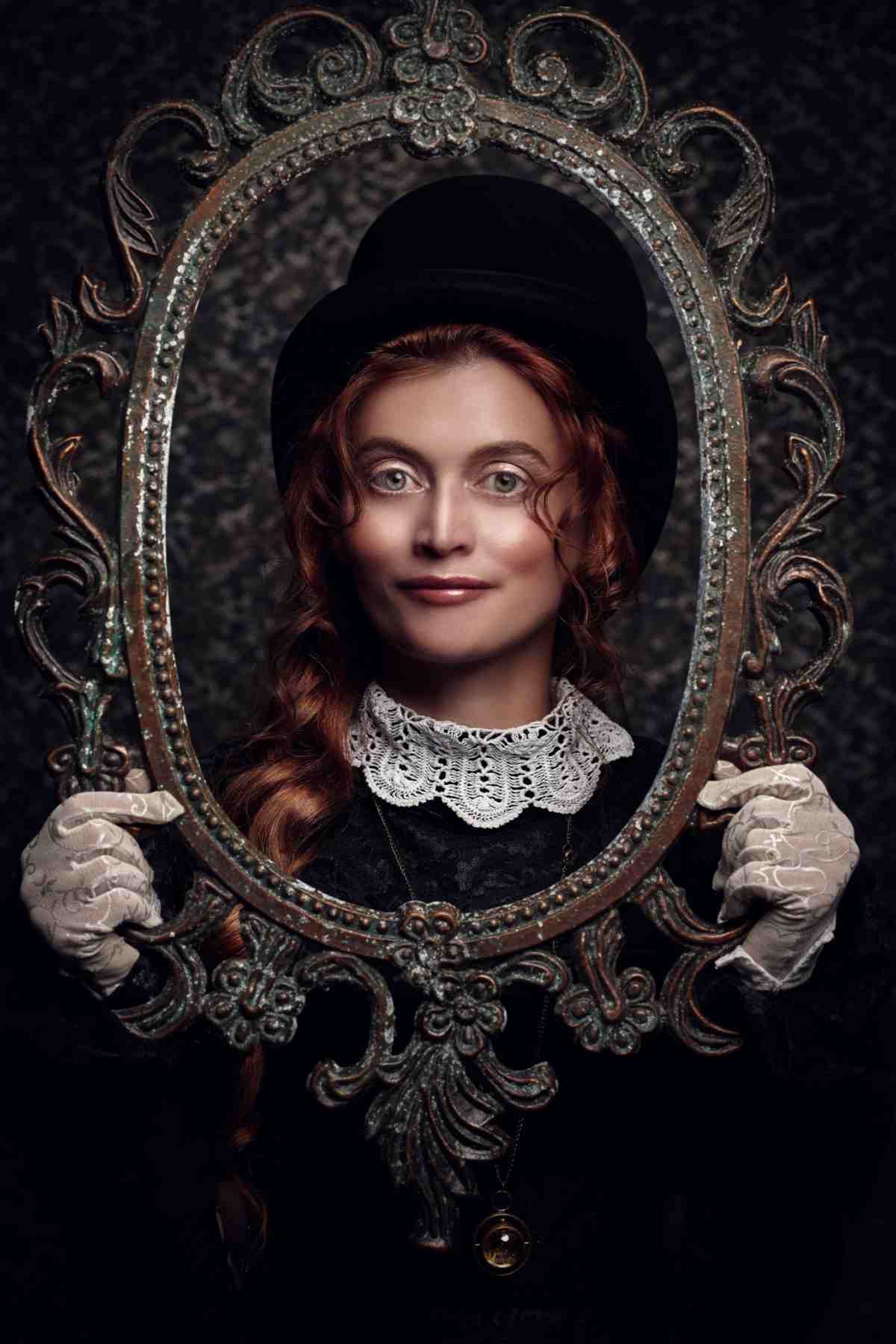 DIY Victorian Costume idea A DIY victorian costume ideas, of a woman dressed in a black dress with lace, with a black top hat, holding a circular victorian frame while wearing white lace gloves.