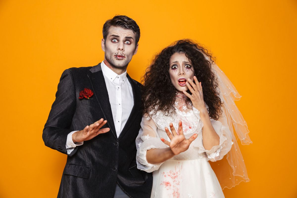 Zombie costume diy A man and woman wearing a diy zombie costume for couples, the man is in a suit with a red carnation on it, and the woman is wearing a wedding dress and veil, both have face paint to make them look like zombies.