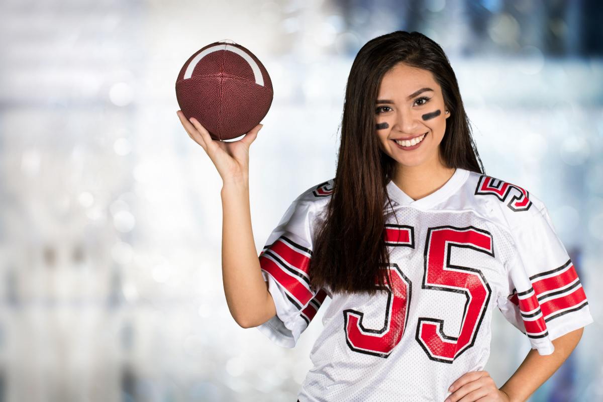 Football player costume A brunette woman holding a football, and wearing a football player costume DIY idea for Halloween, which consists of a jersey and face paint.
