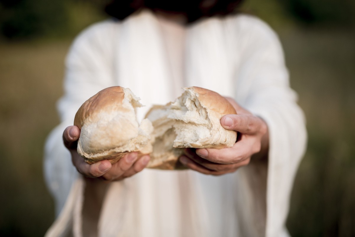 Jesus breaking bread Jesus in a white robe holding a large hot cross bun, and breaking it to symbolize sharing bread with others and to show the religious hot cross buns symbolism.