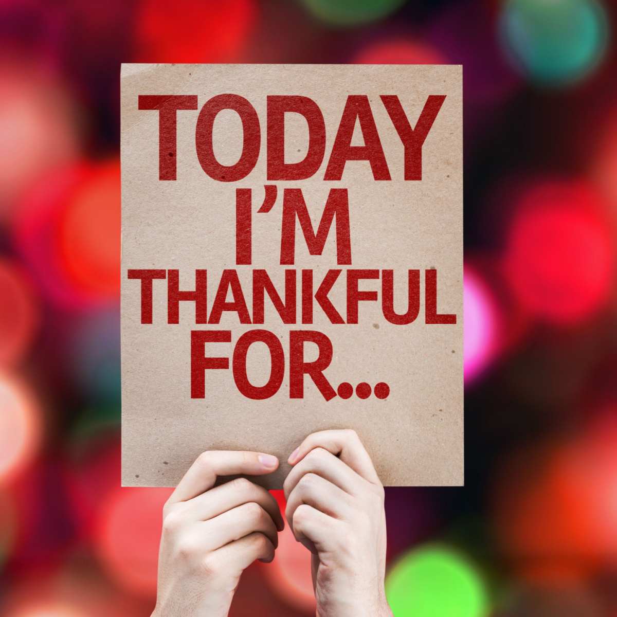 Thankful sign A person's hands holding up a beige sign with a gratitude journal prompt that reads "today I'm thankful for..." with a red bokeh in the background.