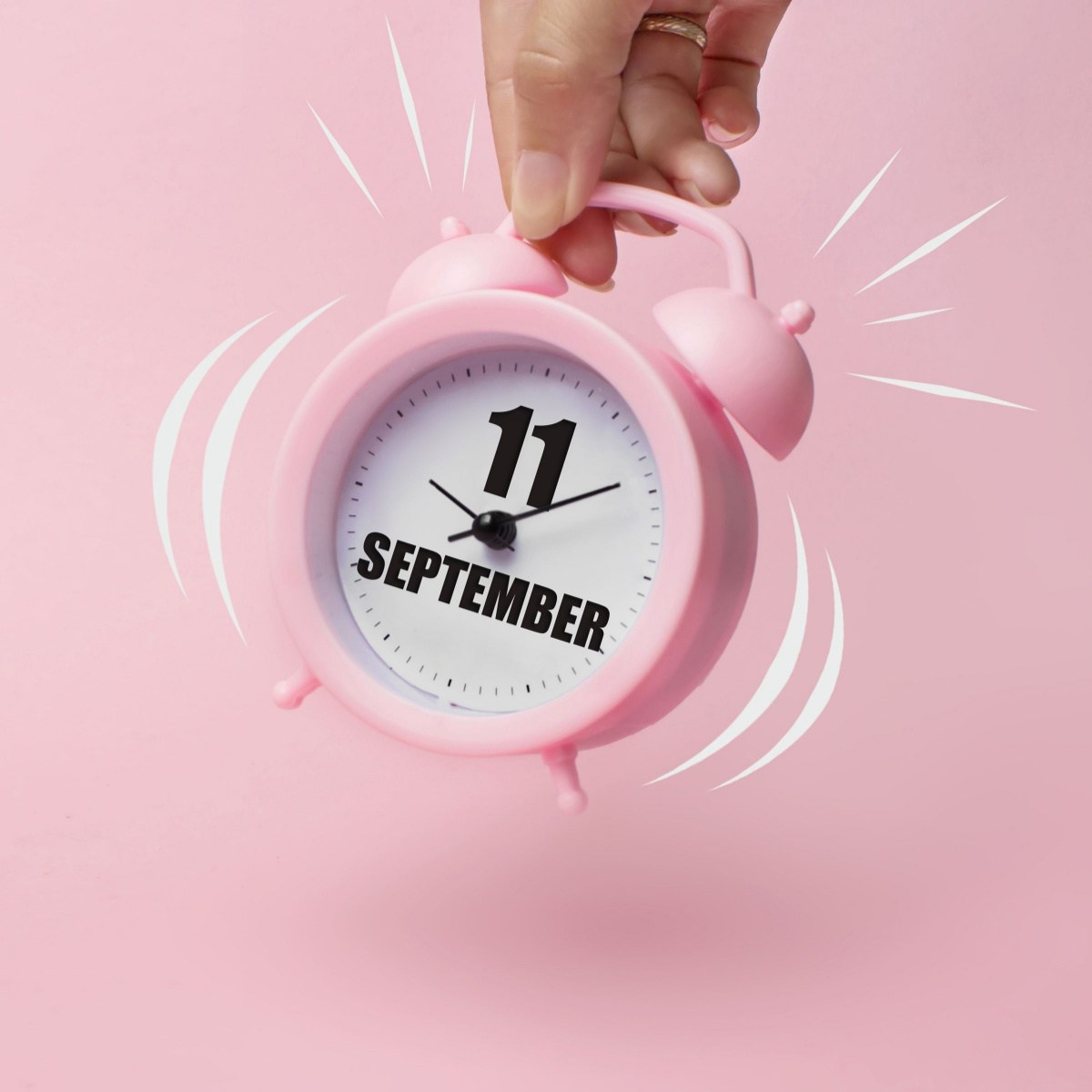 September 11 alarm clock A hand holding a pink alarm clock ringing with "September 11" printed on the middle of it in bold lettering.