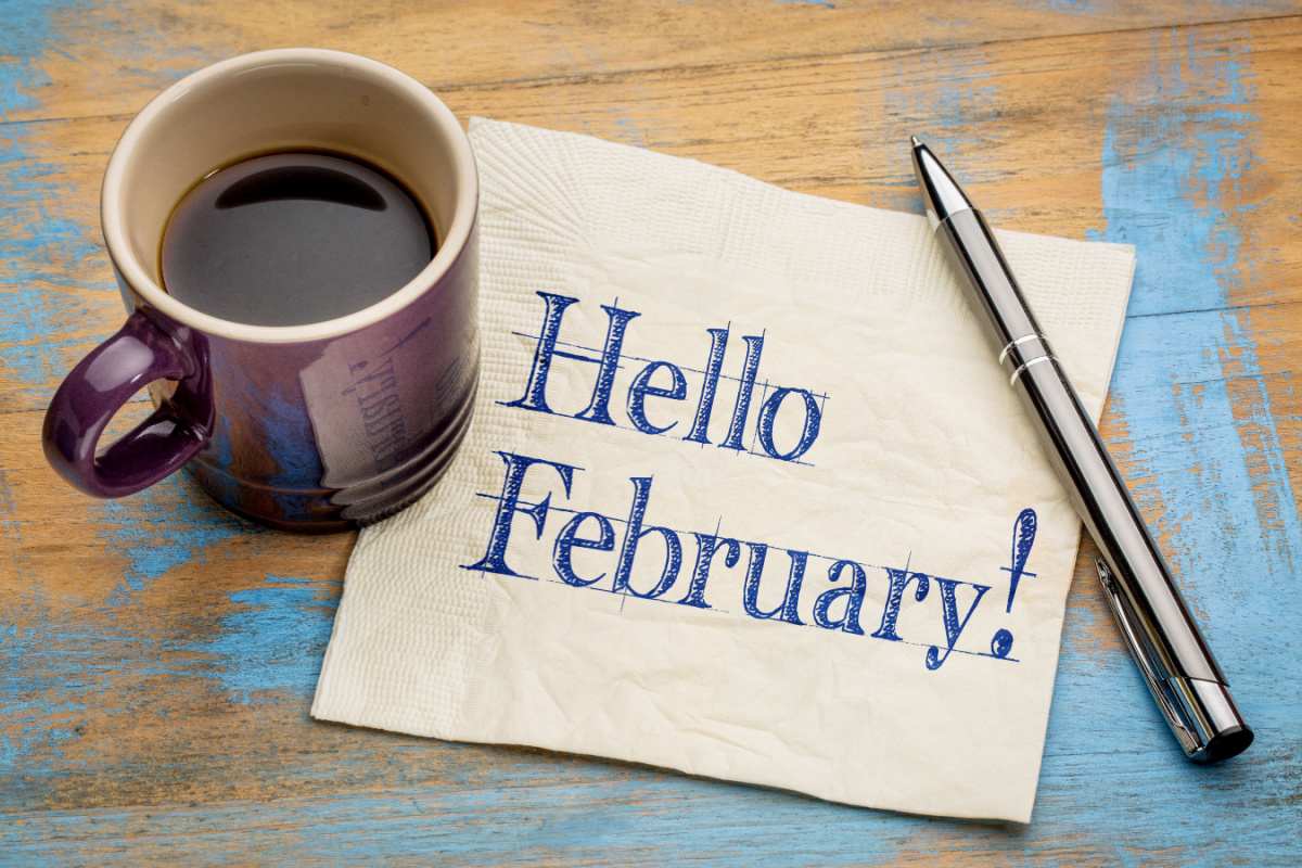 Coffee and hello February napkin A piece of paper that reads "Hello February" with a coffee on top of it, and a pen to the right of it.
