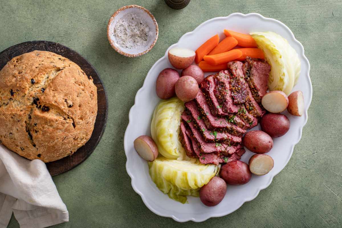 Irish soda bread and corned beef and cabbage with potatoes Traditional Irish foods eaten on St. Patrick's Day arranged on a grey background; a loaf of Irish soda bread is on the left, and a plate of corned beef and cabbage with potatoes is on the right.