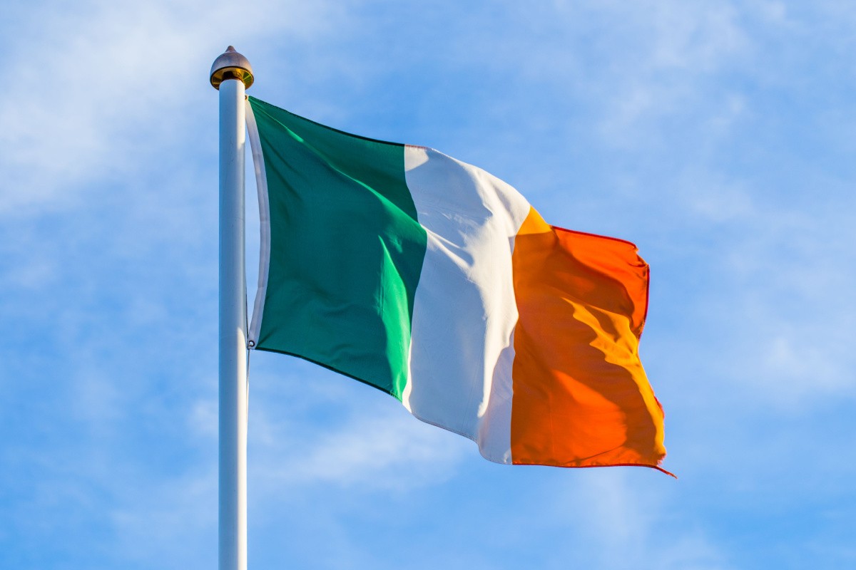 Irish flag on a flagstaff A tricolor Irish flag composed of the Irish flag colors, in order: green, white and orange vertical stripes of equal size attached to a flagstaff, blowing in the wind.
