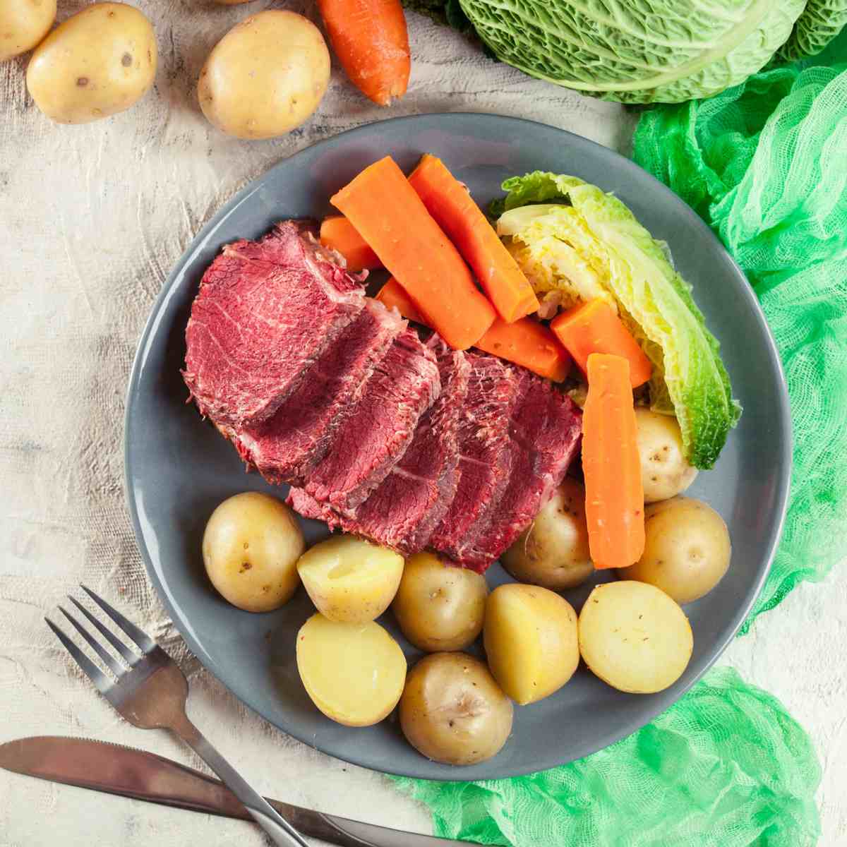 Corned beef and cabbage recipe with potatoes A plate of corned beef and cabbage and potatoes with vegetables, silverware and a green cloth around it to celebrate this St. Patrick's Day dinner.