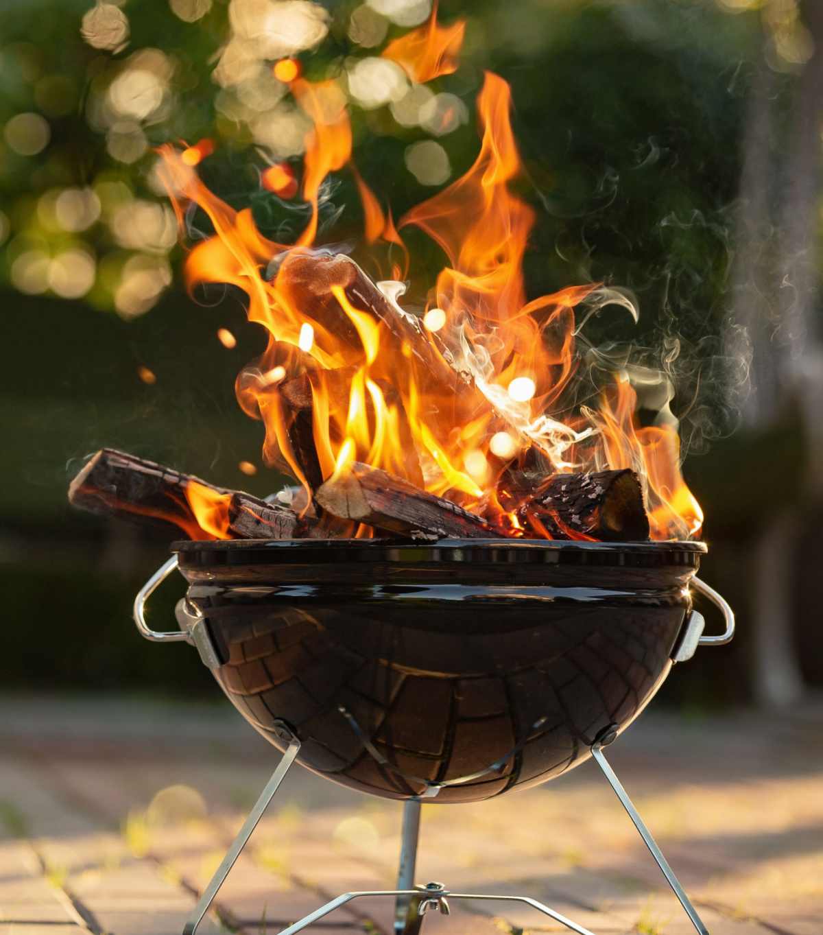 Charcoal grill with large fire A charcoal grill on fire in the summer on a brick patio, where the grillmaster was not using grilling safety tips to keep the flames low.