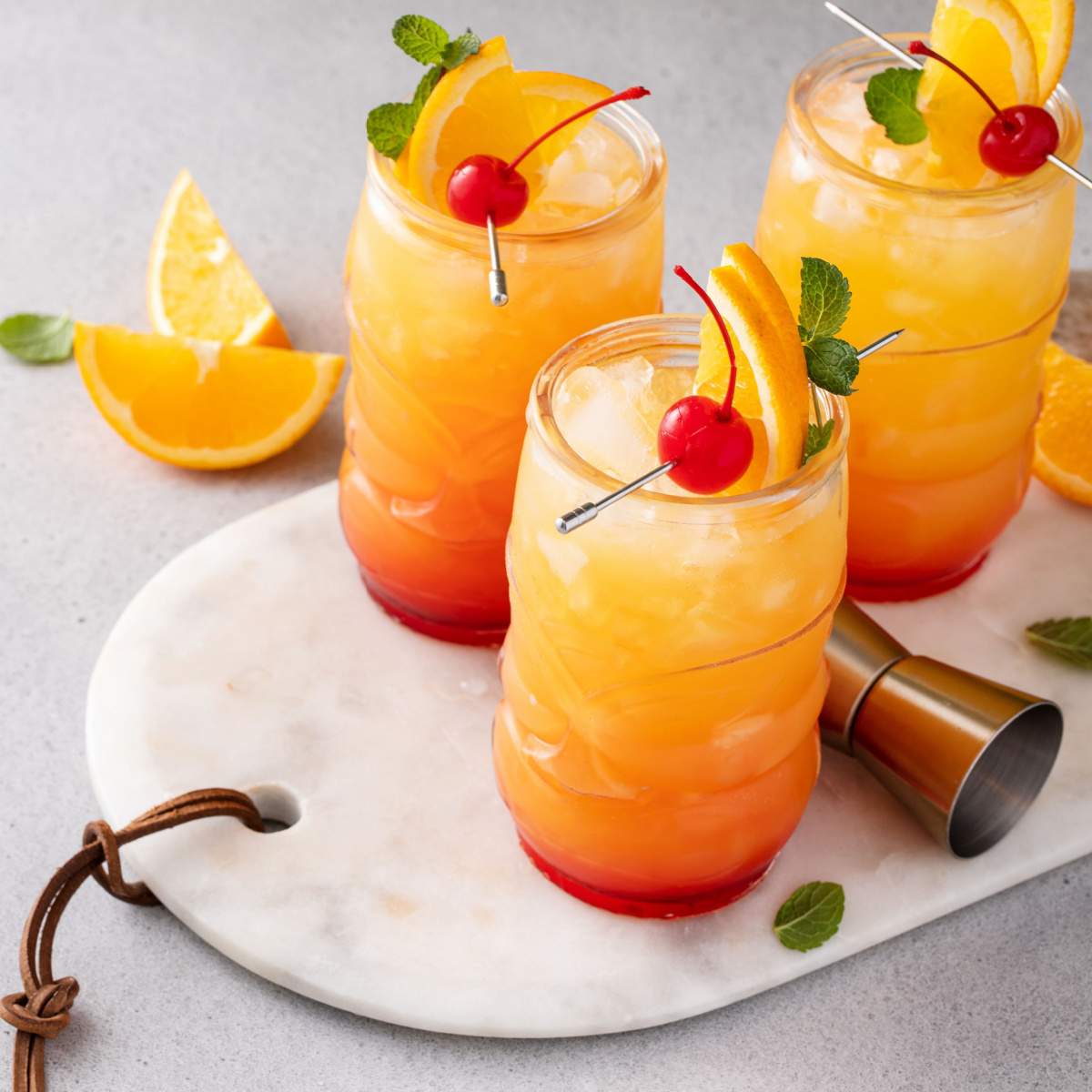 Three mai tais Three mai tai rum cocktails on a marble cutting board, each one is garnished with an orange slice and maraschino cherry on top. with o