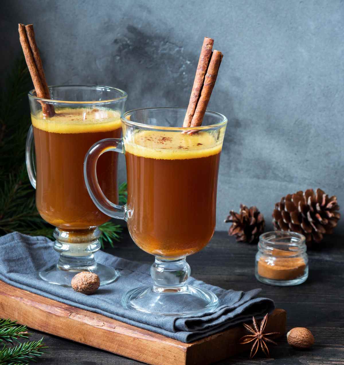 Hot buttered rum Two glass mugs of hot buttered rum made with dark rum garnished with cinnamon sticks on a slate board styled with fall decor around them like pinecones.