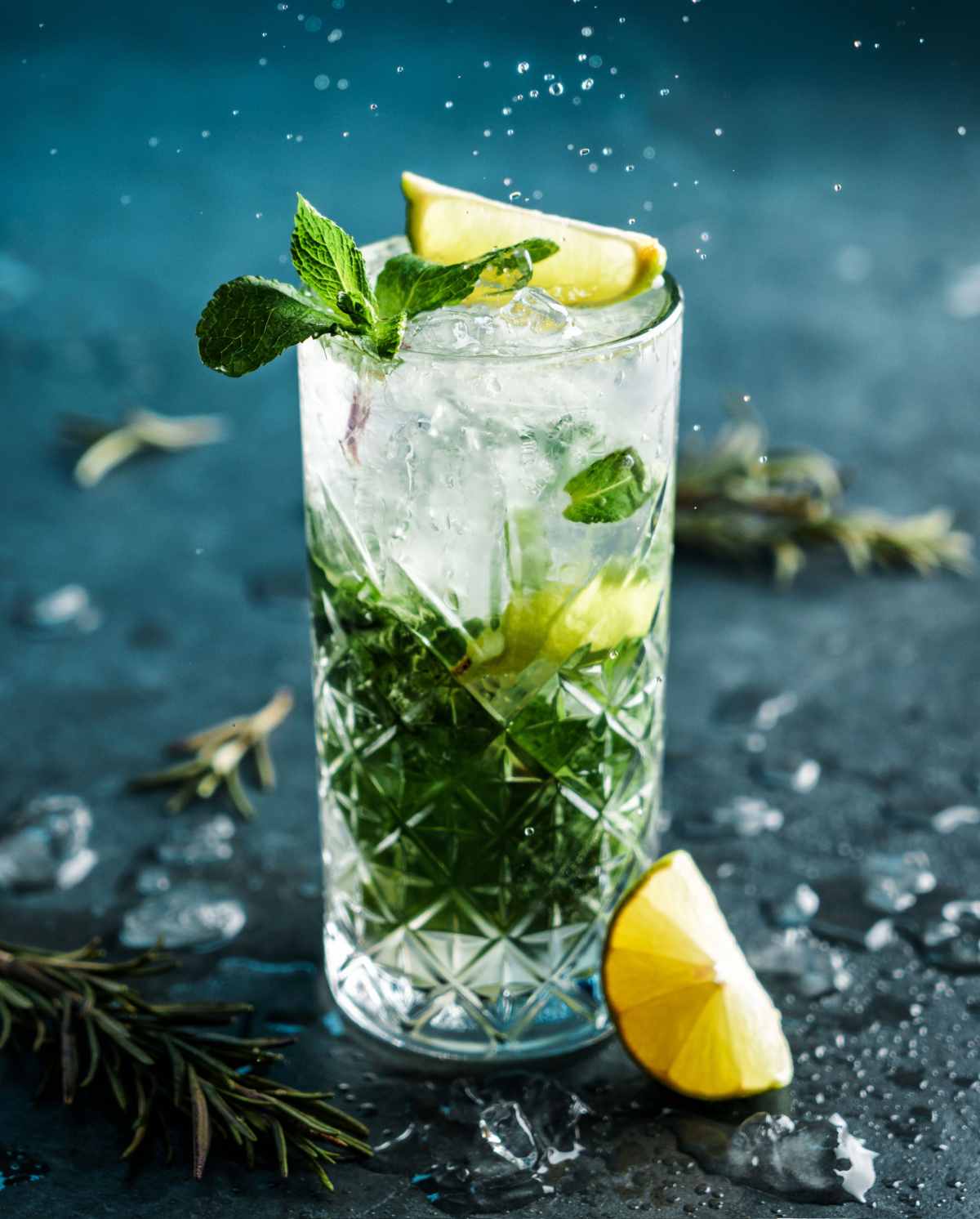 Mojito cocktail A mojito made with white rum garnished with mint and lime, on a teal tabletop with ice and a slice of lime around it.