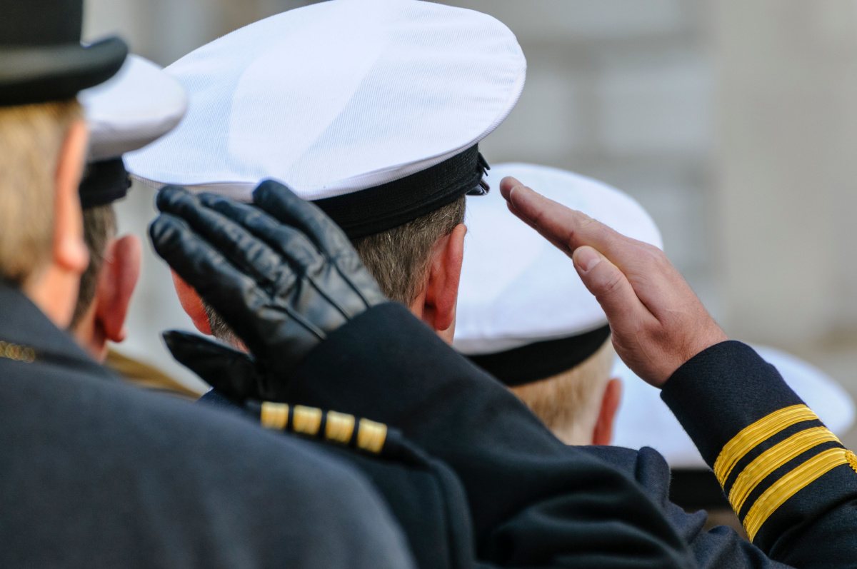 A close up picture taken behind a line of naval officers saluting.