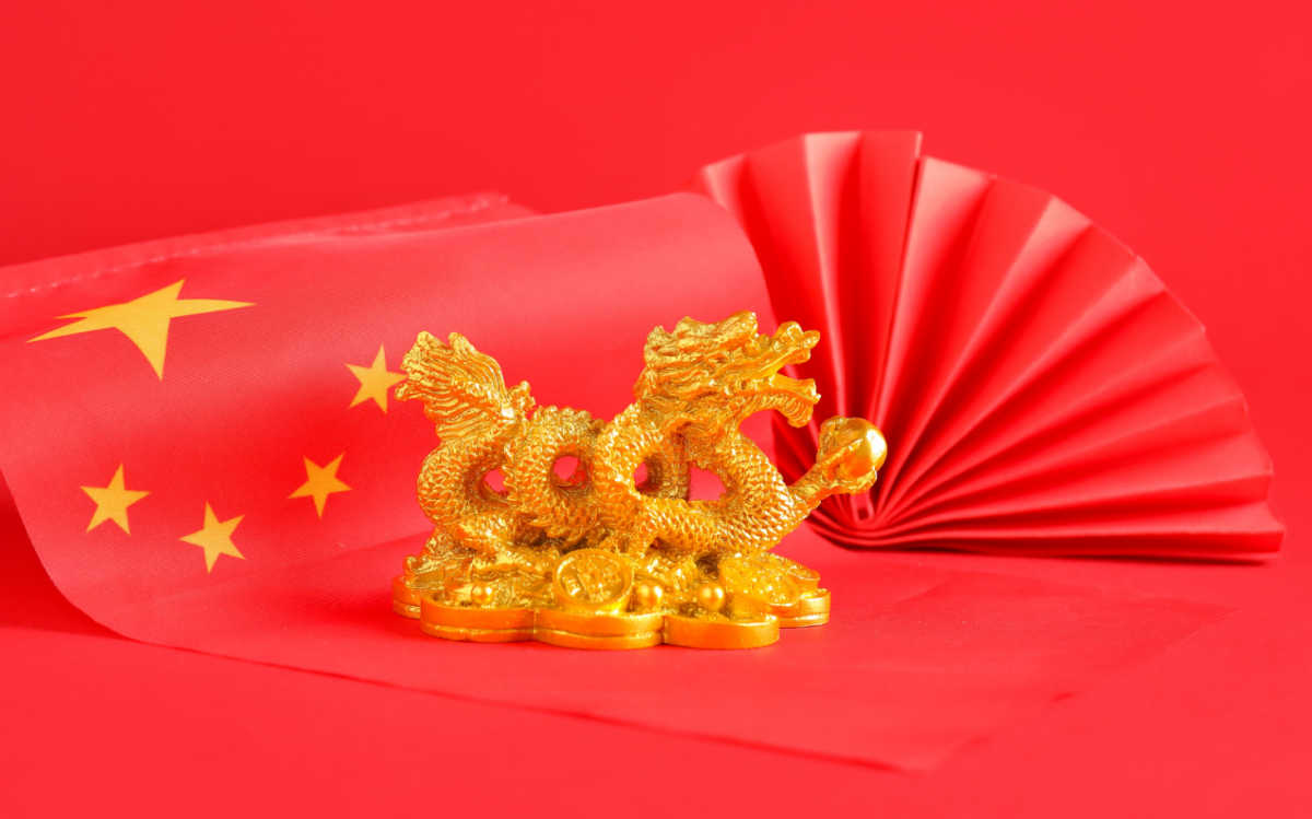 The dragon is a symbol of Chinese culture. Gold dragon statue near a red paper fan and Chinese flag.